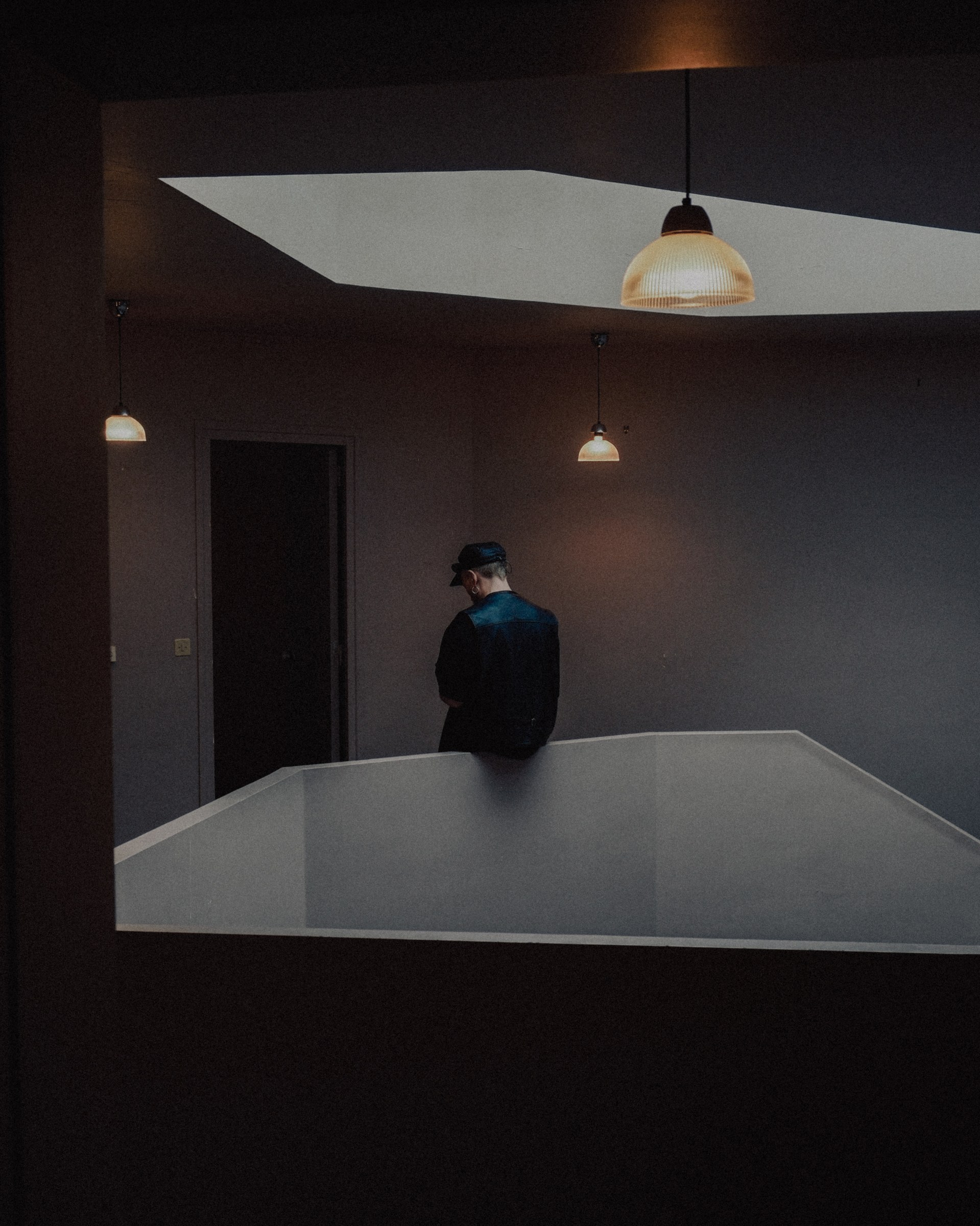 Silhouette en casquette et veste de cuir bleue, pi&egrave;ce sombre &eacute;clair&eacute;e par des suspensions