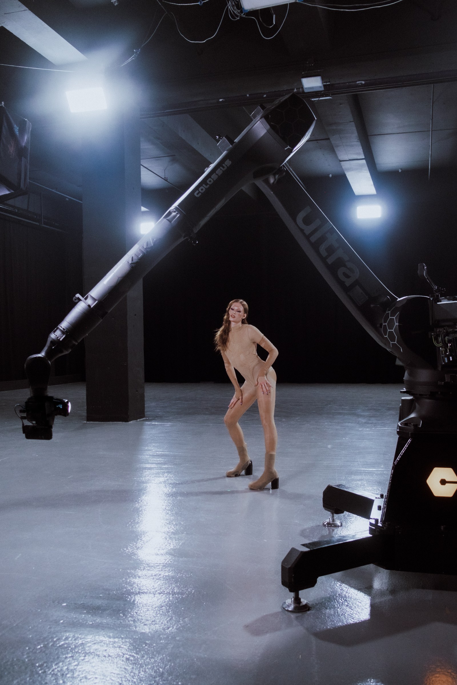 Mod&egrave;le en combinaison couleur chair pos&eacute;e sous un bras robotis&eacute; de cam&eacute;ra en studio