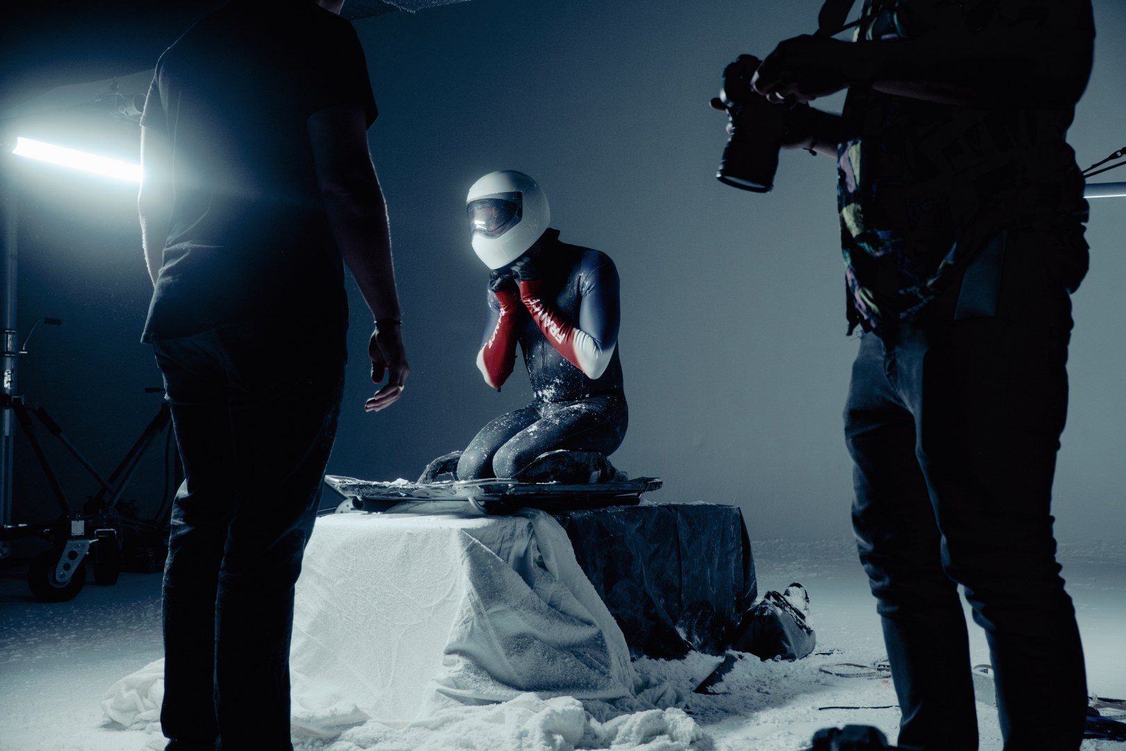 Athl&egrave;te en combinaison de bobsleigh casqu&eacute;e, &eacute;quipe technique filmant en studio recouvert de neige artificielle
