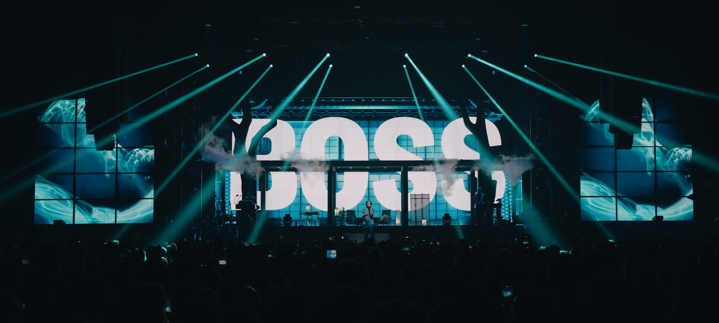 Orelsan sur sc&egrave;ne devant l'inscription BOSS, faisceaux de lumi&egrave;re turquoise