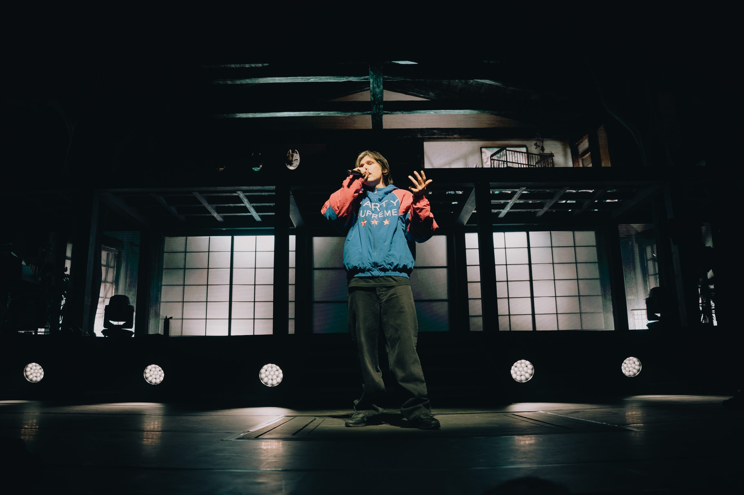 Orelsan en veste bleue et rose, bras lev&eacute;s sur sc&egrave;ne