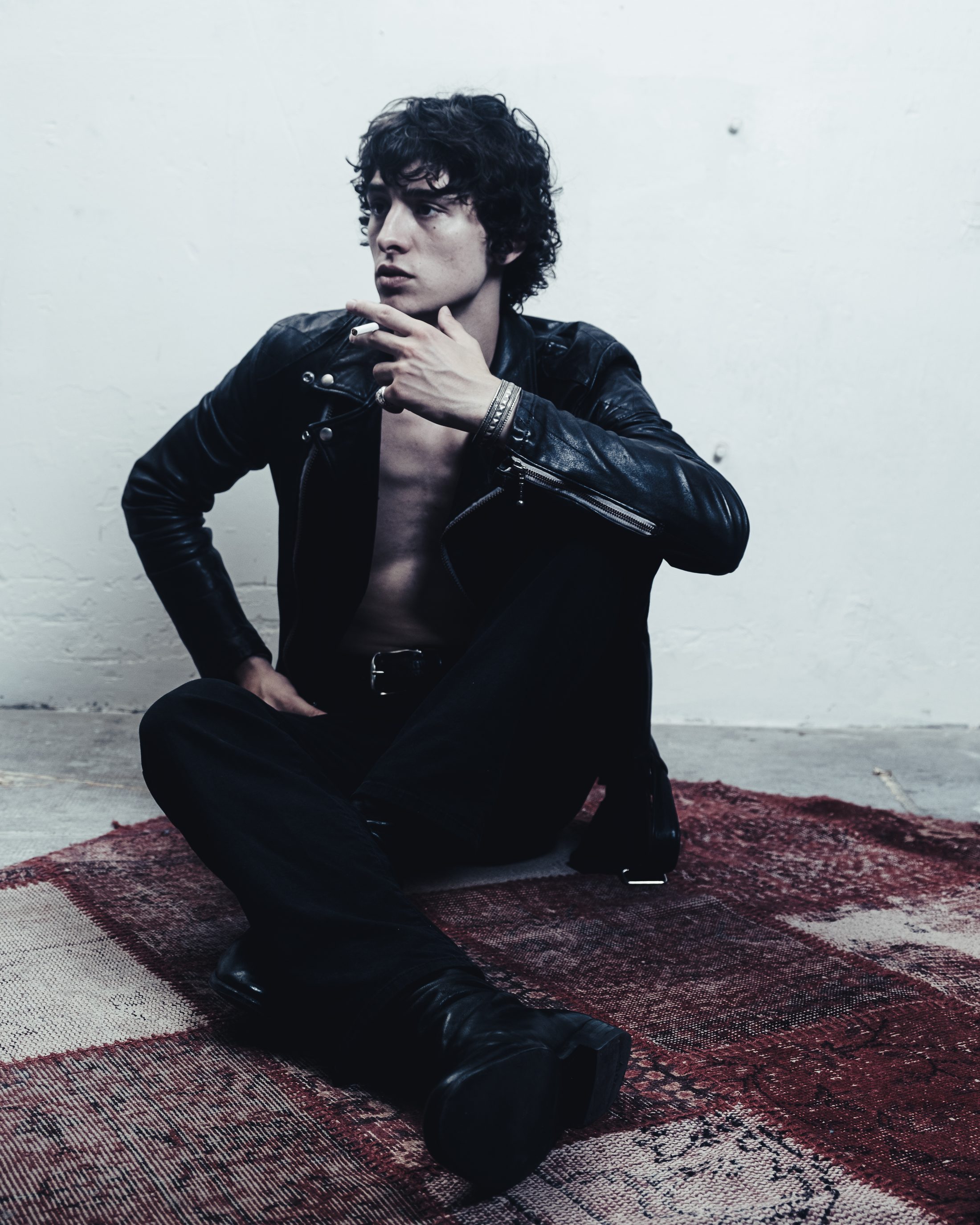 Assis sur un tapis, blouson de cuir, cigarette