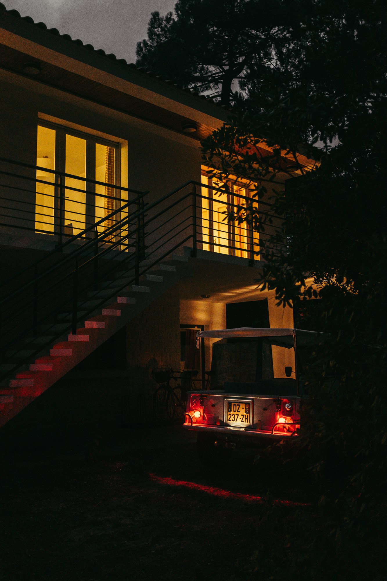 Maison illumin&eacute;e la nuit, voiture aux phares rouges