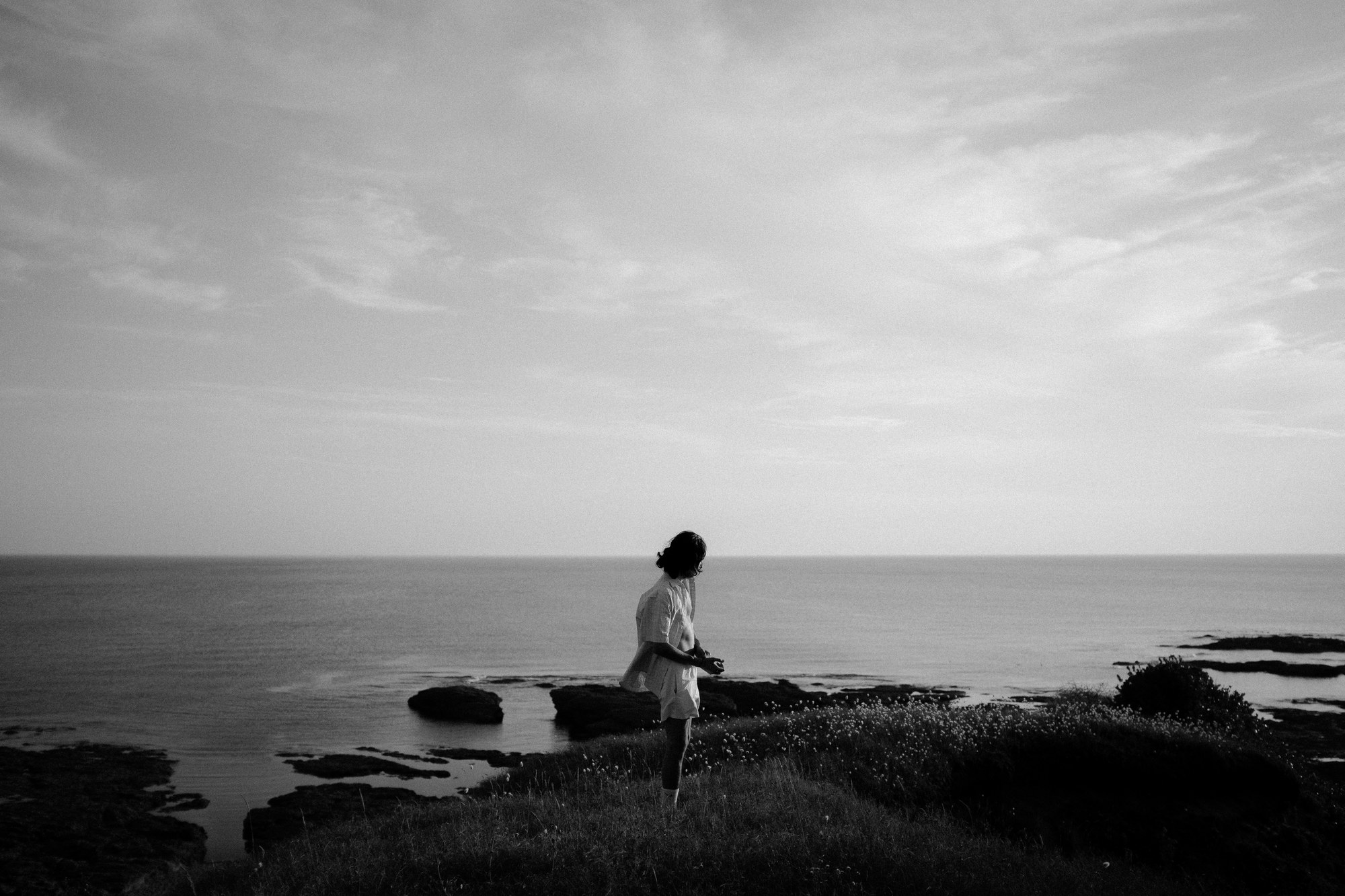Femme assise sur les rochers face &agrave; la mer, noir et blanc